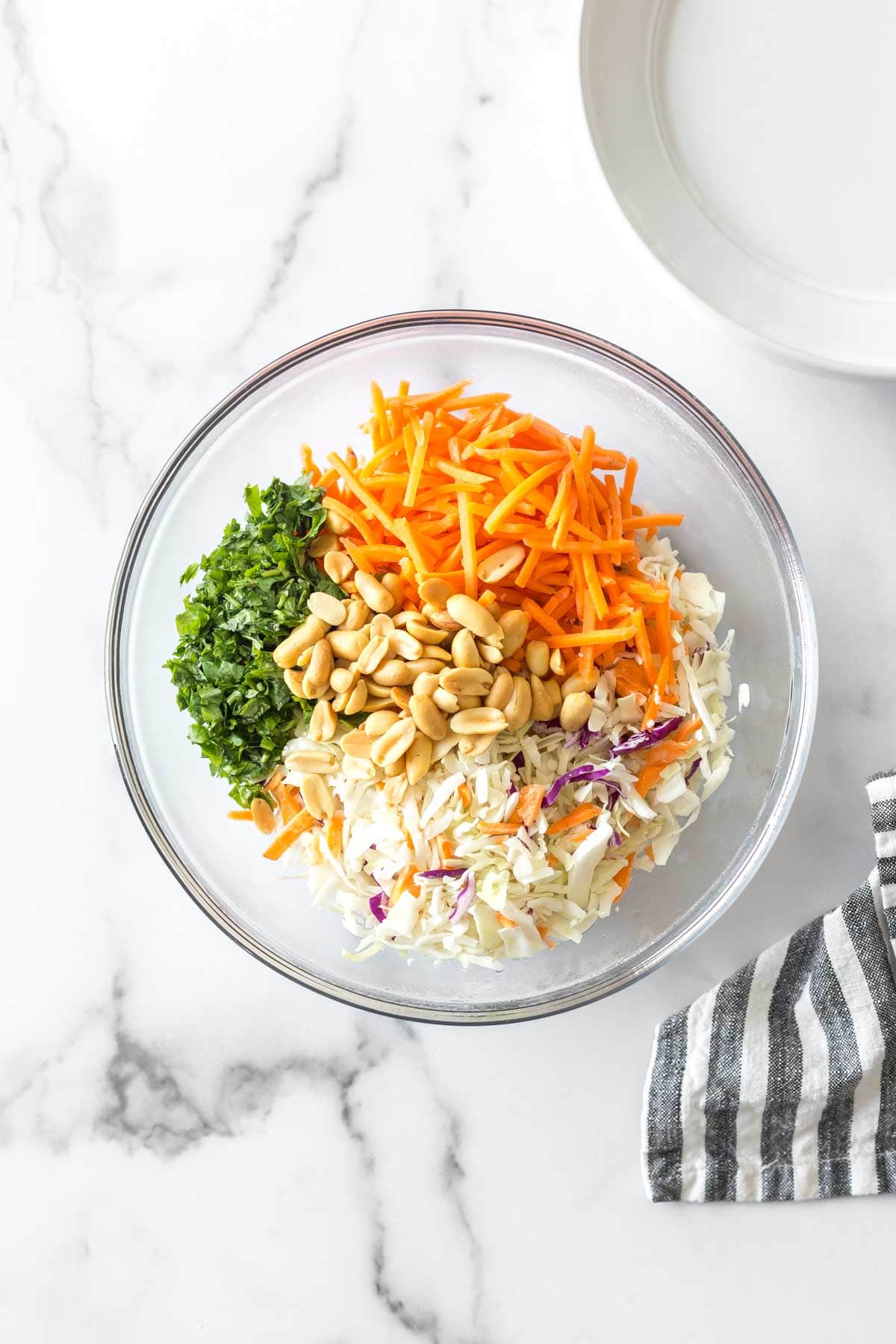 ingredients for asian chicken wrap recipe in a large glass bowl: shredded coleslaw, carrots, cilantro and peanuts