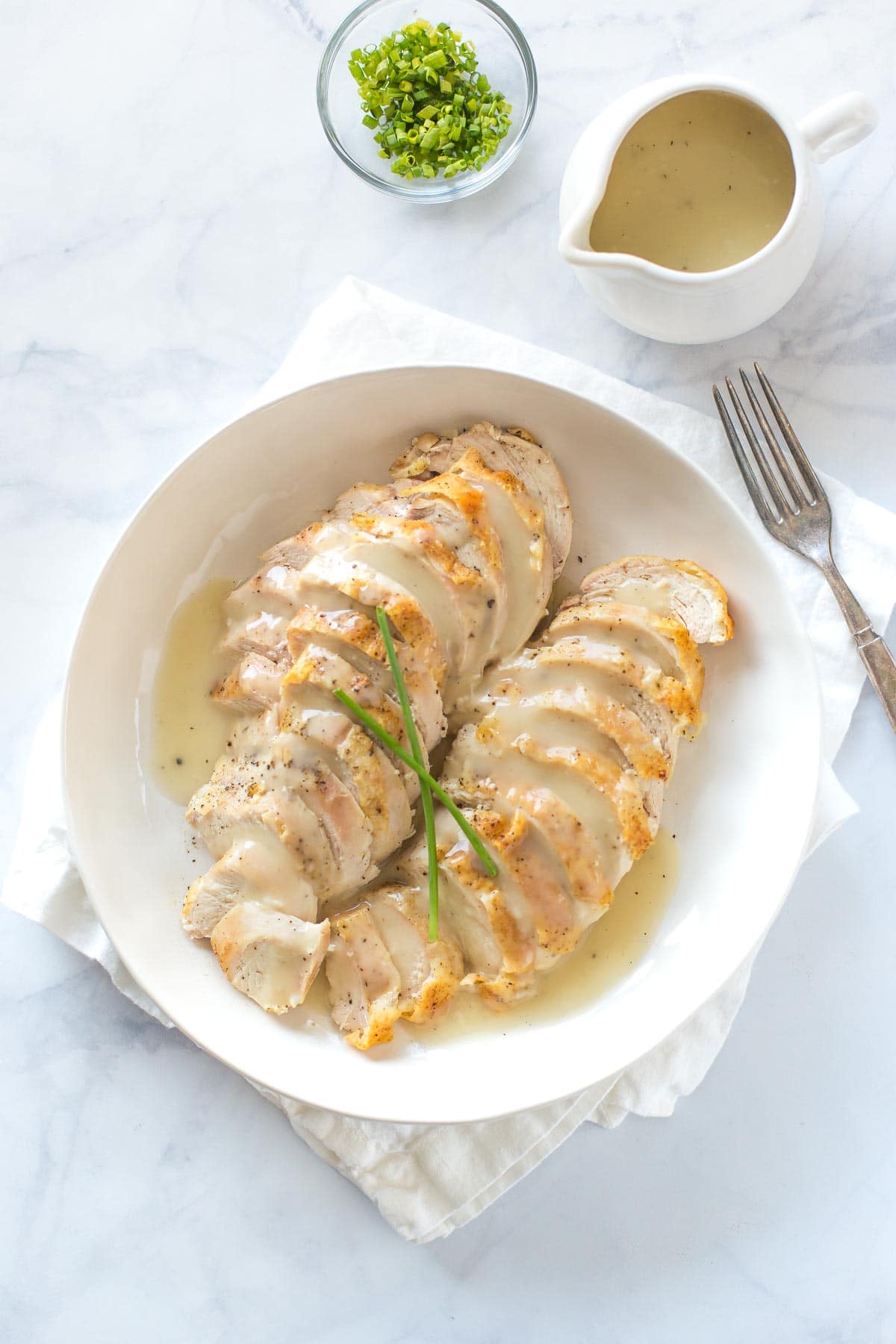 aerial view of sliced chicken breast topped with chicken veloute sauce in a shallow cream bowl on white marble surface