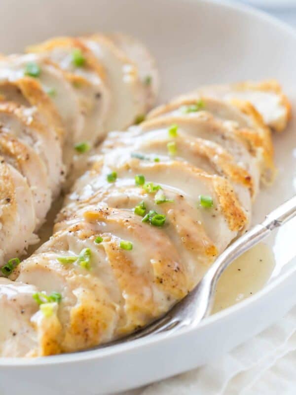 close up of sliced chicken breast topped with chicken veloute sauce in a shallow cream bowl on white marble surface