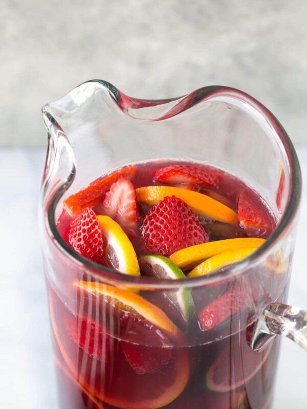 close up of a pitcher of red sangria with fresh fruit on a bright white background