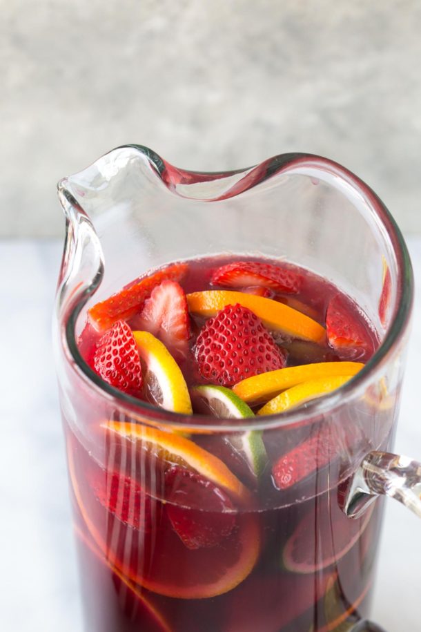 close up of a pitcher of red sangria with fresh fruit on a bright white background