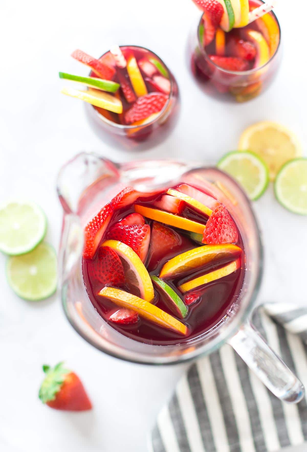 aerial view of a pitcher of red sangria with fresh fruit on a bright white background