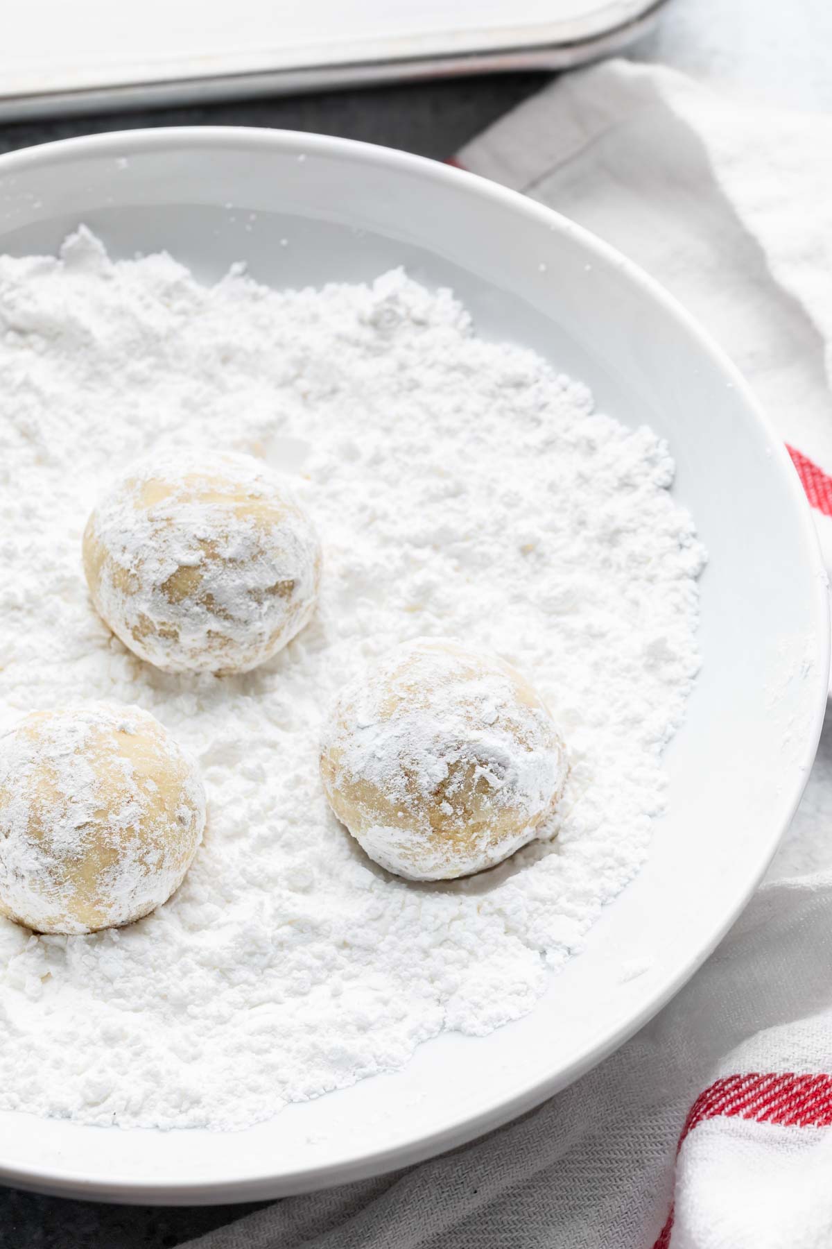 3 pecan snowball cookies in a bowl of powdered sugar