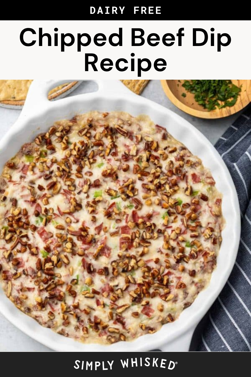 Round white dish filled with creamy chipped beef dip, topped with chopped pecans and green onions, sitting next to a small bowl of herbs and a striped napkin. Text above reads Chipped Beef Dip Recipe.