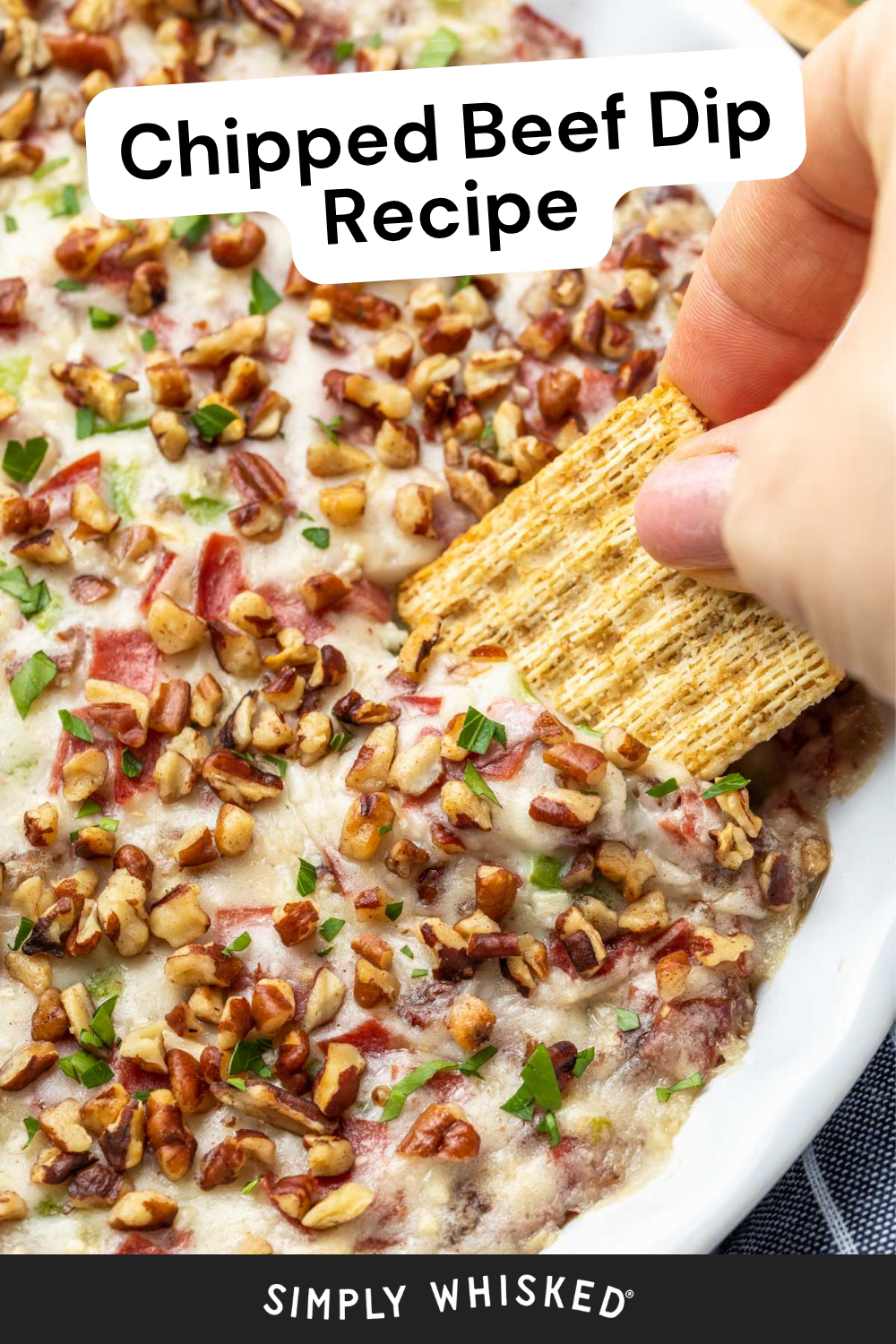 A hand dips a cracker into a creamy chipped beef dip topped with chopped pecans, served in a white dish. The text reads, Chipped Beef Dip Recipe.
