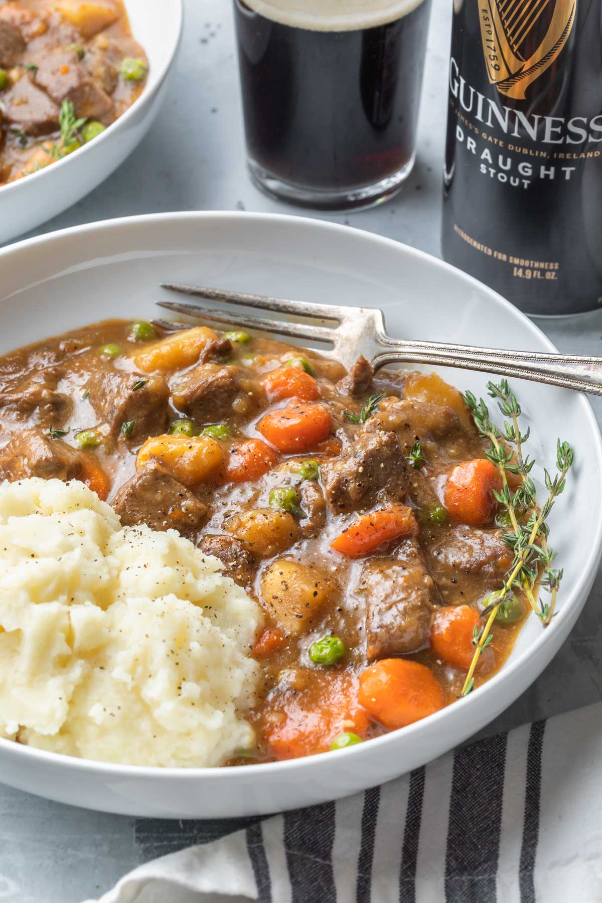 irish beef stew in a bowl with mashed potatoes garnished with fresh thyme