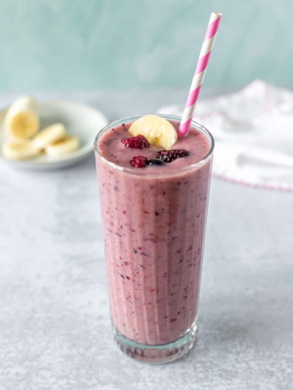berry banana smoothie garnished with a pink and white paper straw, frozen berries and a banana slice