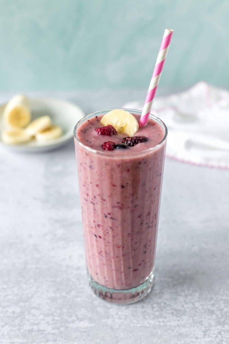 berry banana smoothie garnished with a pink and white paper straw, frozen berries and a banana slice