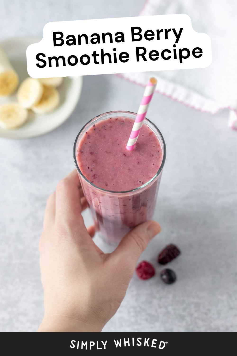 A hand holds a glass of vibrant banana berry smoothie with a pink-striped straw. Sliced bananas and berries sit nearby. Text reads: Banana Berry Smoothie Recipe.