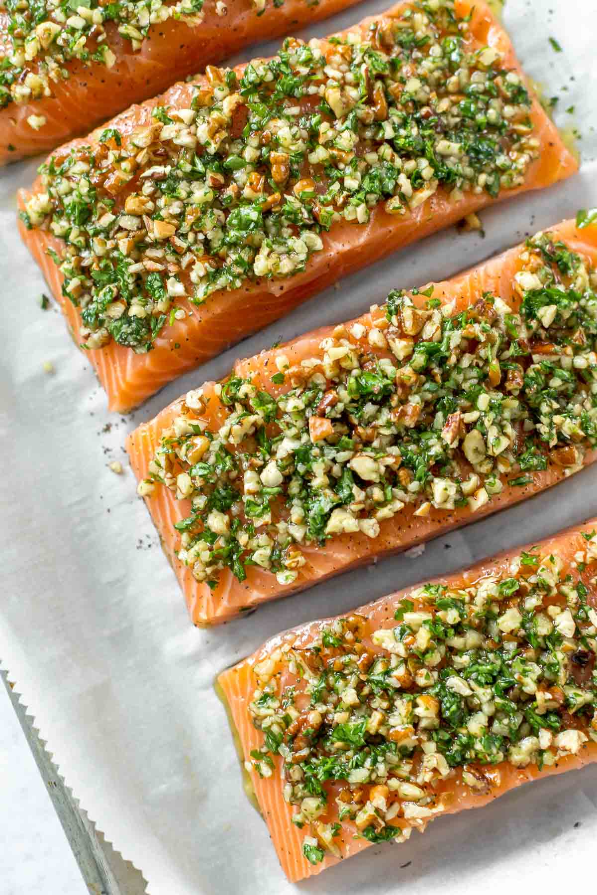 Raw salmon with nuts and herbs spread on top, prepared to be baked on a parchment lined baking sheet.