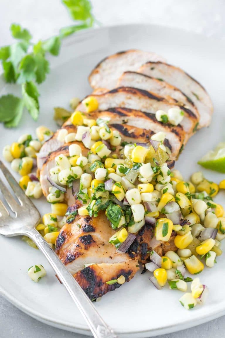 tequila lime chicken topped with corn salsa on a light gray plate, vintage fork and cilantro sprig on the side of the plate