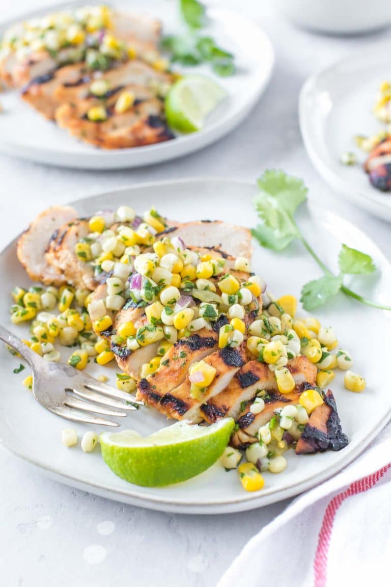 tequila lime chicken topped with corn salsa on a light gray plate, vintage fork and lime wedge on the side of the plate