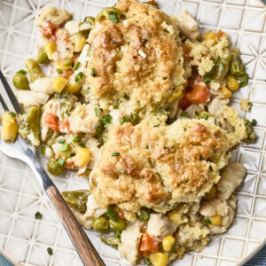 A plate with two servings of easy chicken pot pie with biscuits, filled with chunks of chicken, peas, carrots, corn, and green beans in a creamy sauce. A fork rests on the edge of the plate.