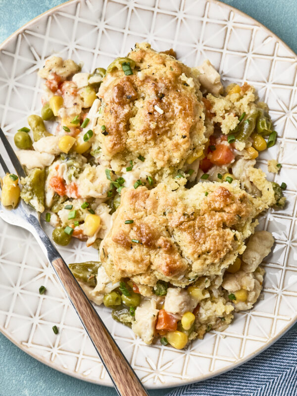 A plate with two servings of easy chicken pot pie with biscuits, filled with chunks of chicken, peas, carrots, corn, and green beans in a creamy sauce. A fork rests on the edge of the plate.