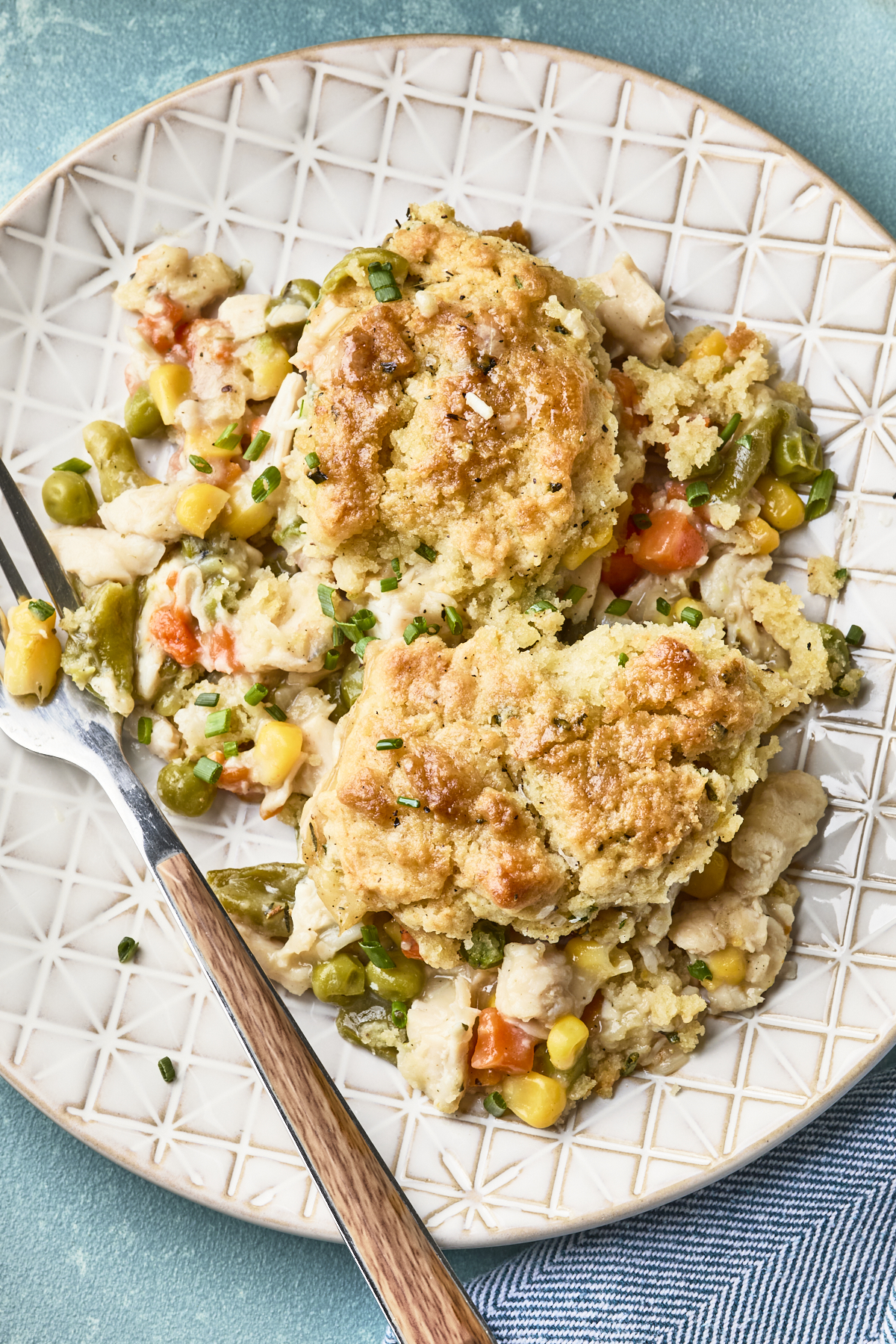 A plate with two servings of easy chicken pot pie with biscuits, filled with chunks of chicken, peas, carrots, corn, and green beans in a creamy sauce. A fork rests on the edge of the plate.