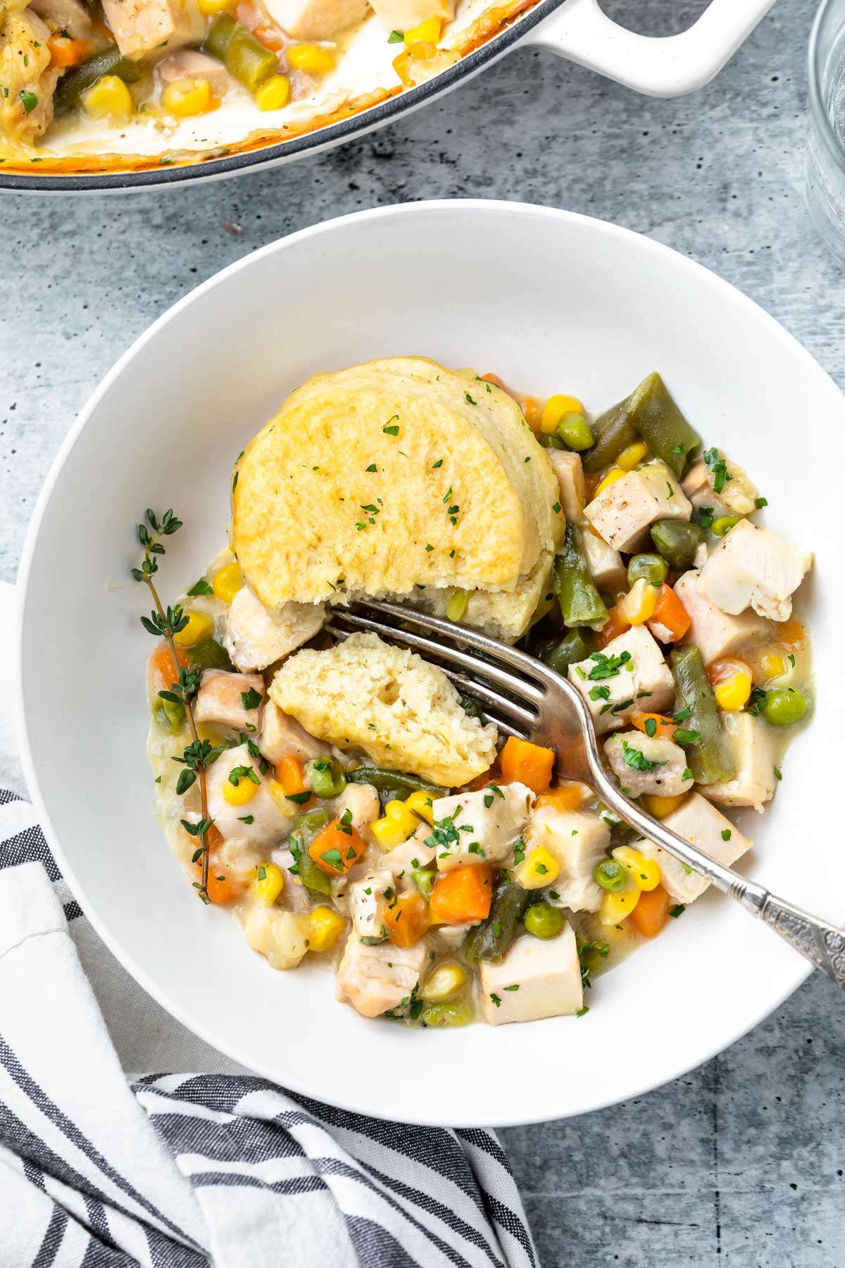 serving of easy chicken pot pie with biscuits in a large white bowl garnished with fresh thyme