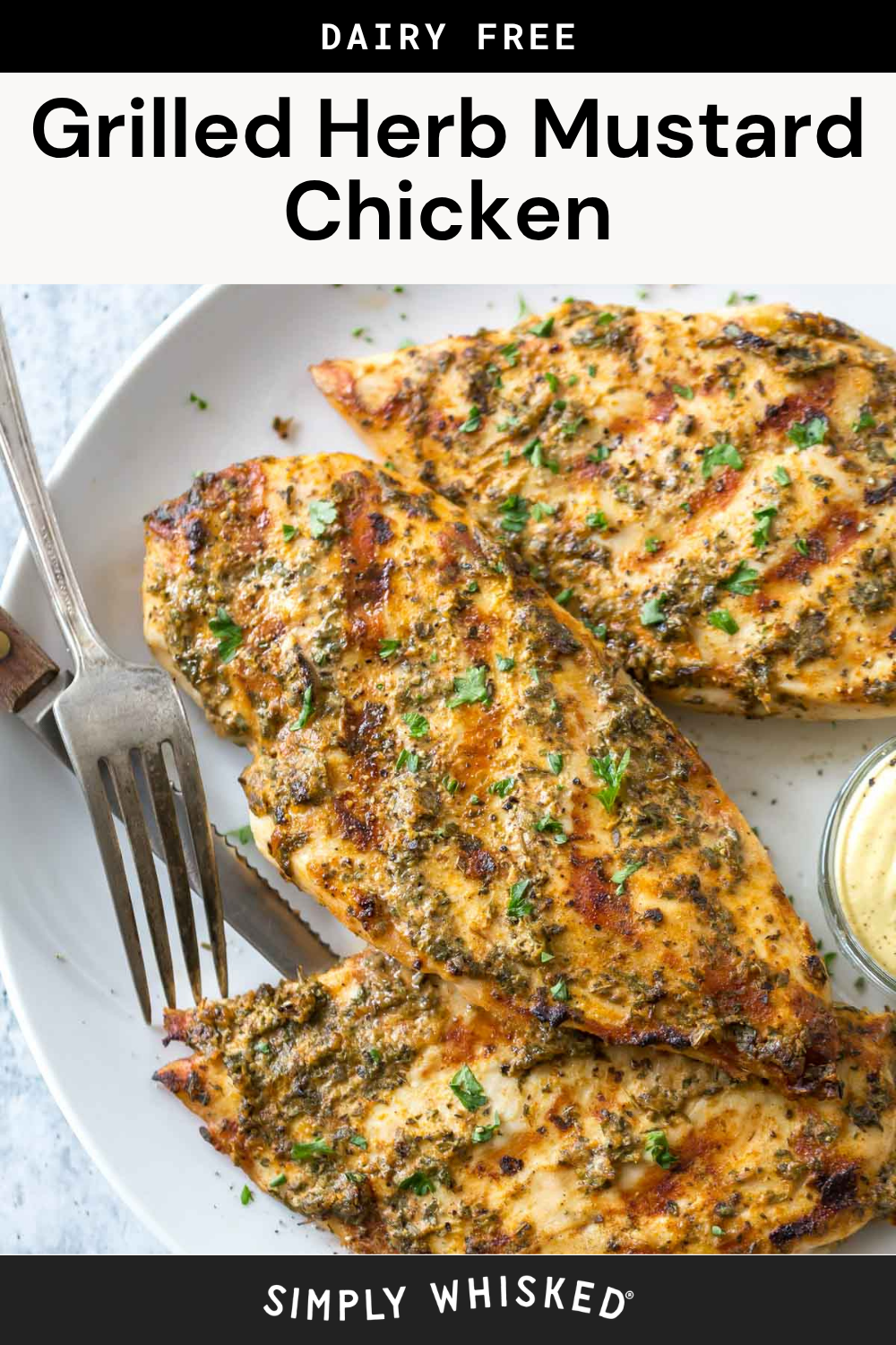Grilled chicken breasts coated in a flavorful green herb mustard chicken marinade, garnished with chopped herbs on a white plate with a fork and a small dish of mustard. Text overlay reads Grilled Herb Mustard Chicken.