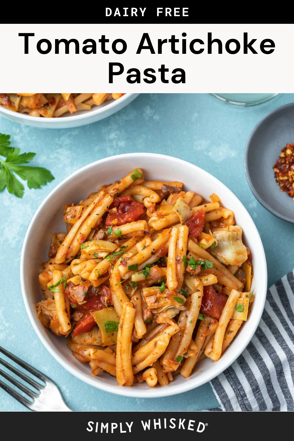 A bowl of artichoke pasta with tomato sauce, fresh herbs, and tender artichokes sits on a blue table next to a fork, striped napkin, and a bowl of red pepper flakes. Text above says Dairy Free Tomato Artichoke Pasta.