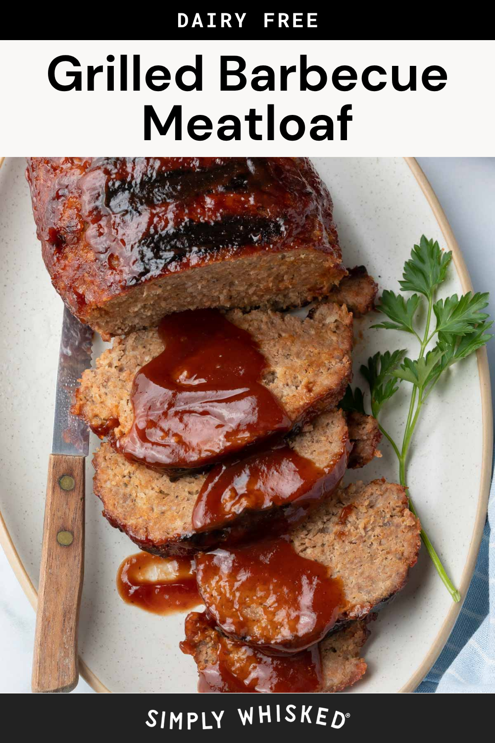 Sliced grilled barbecue meatloaf topped with smoky barbecue sauce, garnished with parsley, served on a white plate with a knife beside it. Text above reads Dairy Free Grilled Barbecue Meatloaf.