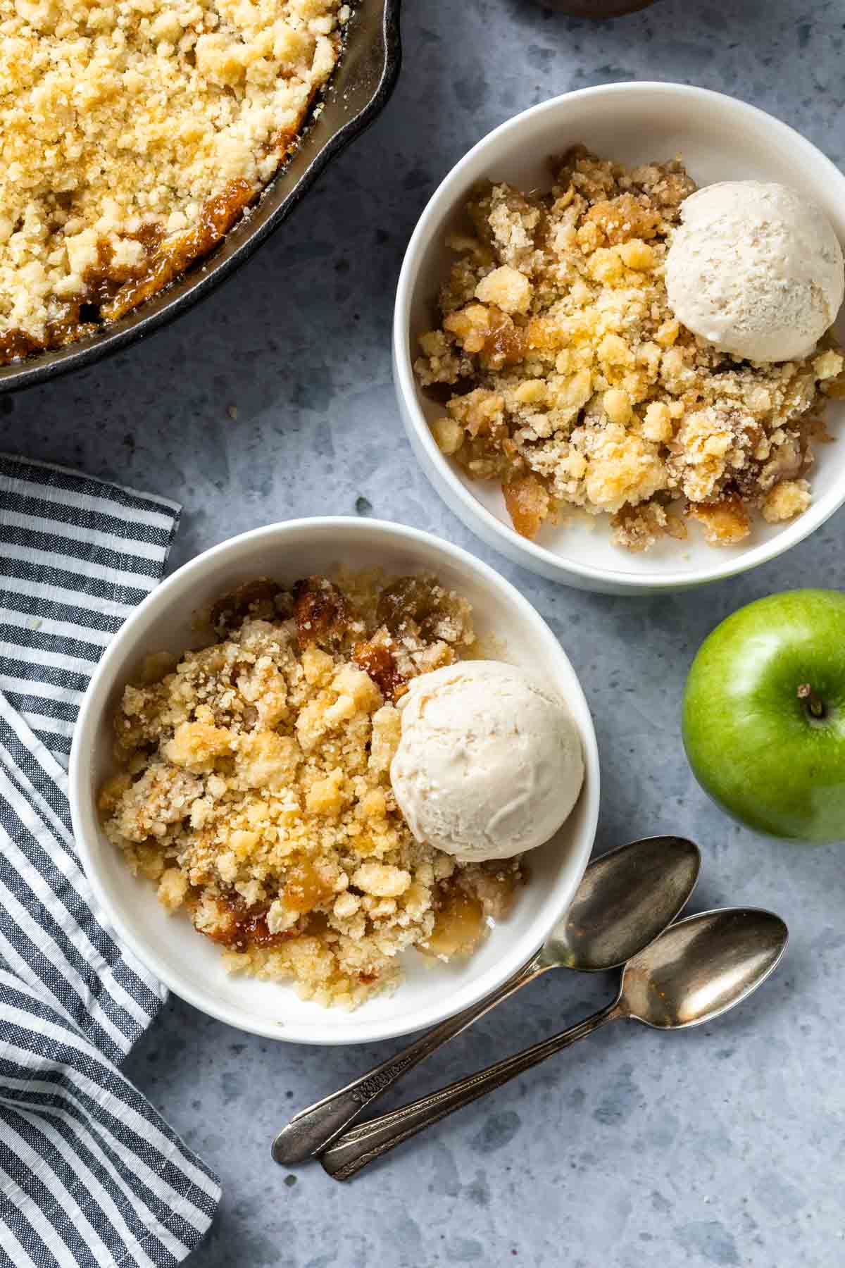 overhead view of two bowls of vegan apple crisp with a scoop of ice-cream on a countertop