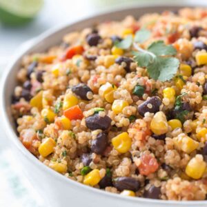 Close up view of Mexican quinoa in a large bowl on a striped napkin with limes and cilantro, on a white background