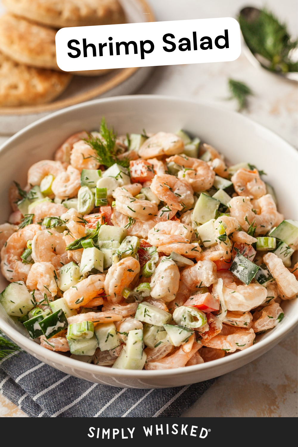 A vibrant bowl of shrimp salad, filled with chopped cucumbers, juicy tomatoes, green onions, and fresh herbs, sits atop a light table with biscuits in the background. The text reads Shrimp Salad and Simply Whisked.