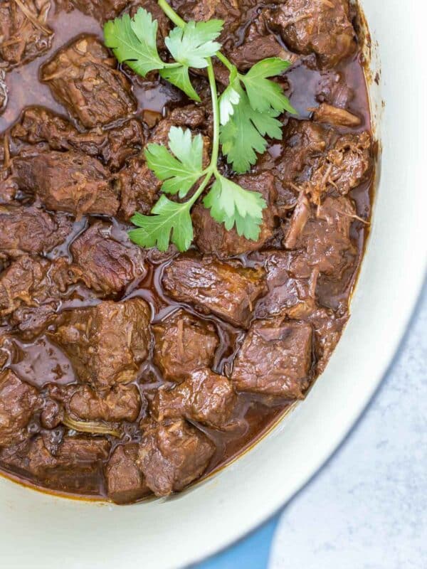 overhead closeup of Guinness braised beef cooked with a sprig of fresh parsley in a blue Dutch oven on a gray background