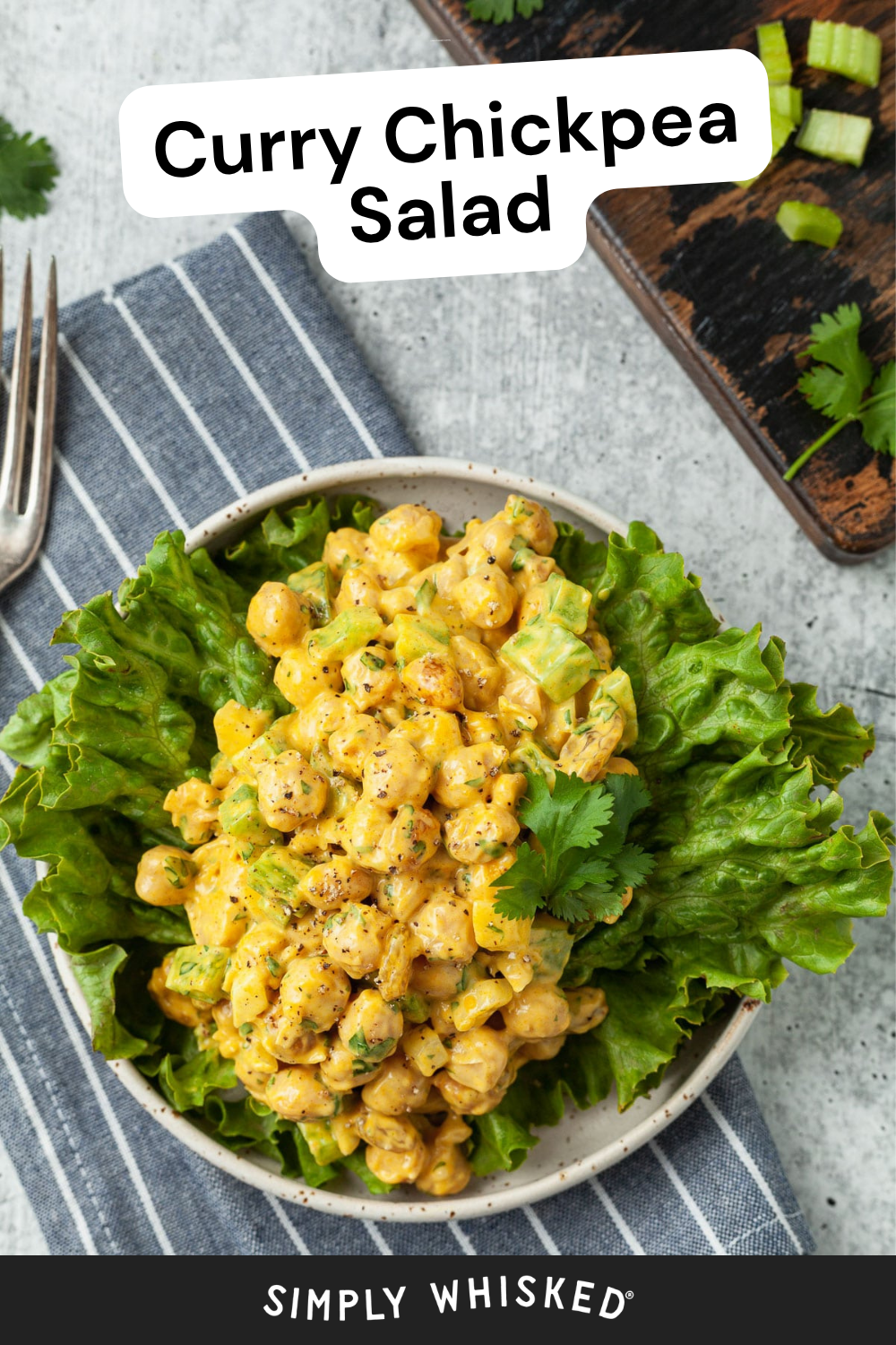 A vibrant bowl of curry chickpea salad sits atop crisp green lettuce, garnished with fresh cilantro. Resting on a striped napkin with a fork beside it, this colorful curry chickpea salad is both inviting and flavorful. Text reads Curry Chickpea Salad at the top and Simply Whisked at the bottom.