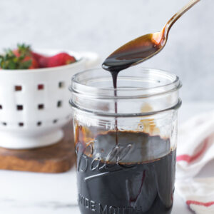 balsamic reduction (balsamic glaze) in a mason jar with a spoon above letting some drip back into the jar
