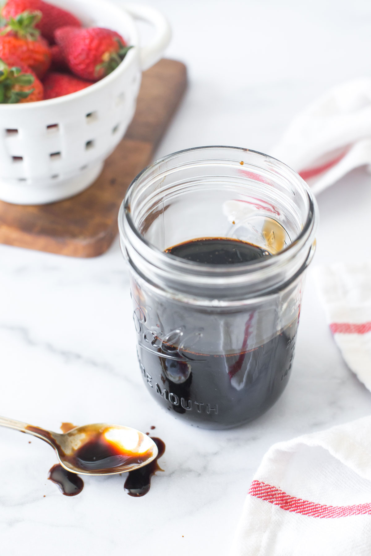 balsamic reduction in a mason jar with a messy spoon covered in the balsamic glaze to the side