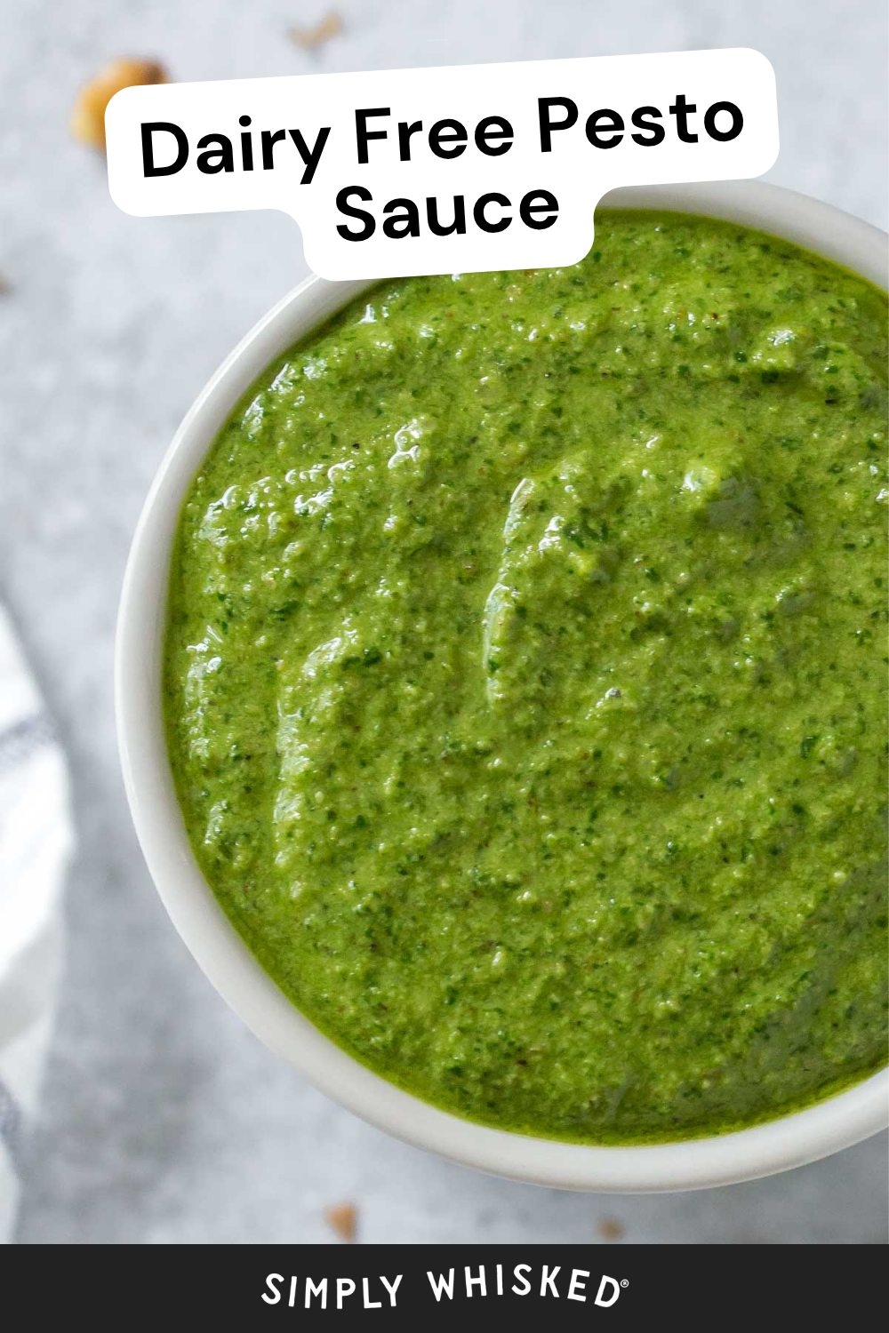 A vibrant bowl of green Dairy Free Pesto Sauce sits on a gray surface. Text at the top reads Dairy Free Pesto Sauce, and at the bottom, Simply Whisked.