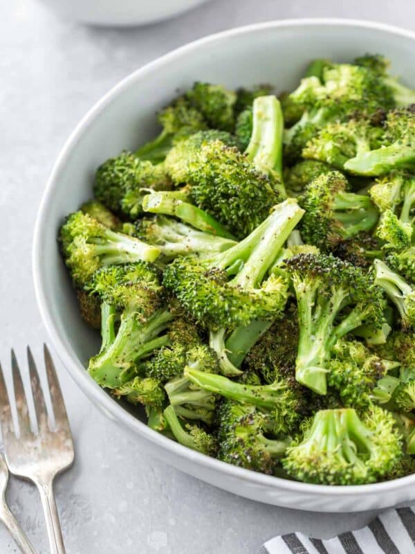 overhead shot of oven roasted broccoli in a serving dish on a gray surface with forks and striped napkin in the foreground
