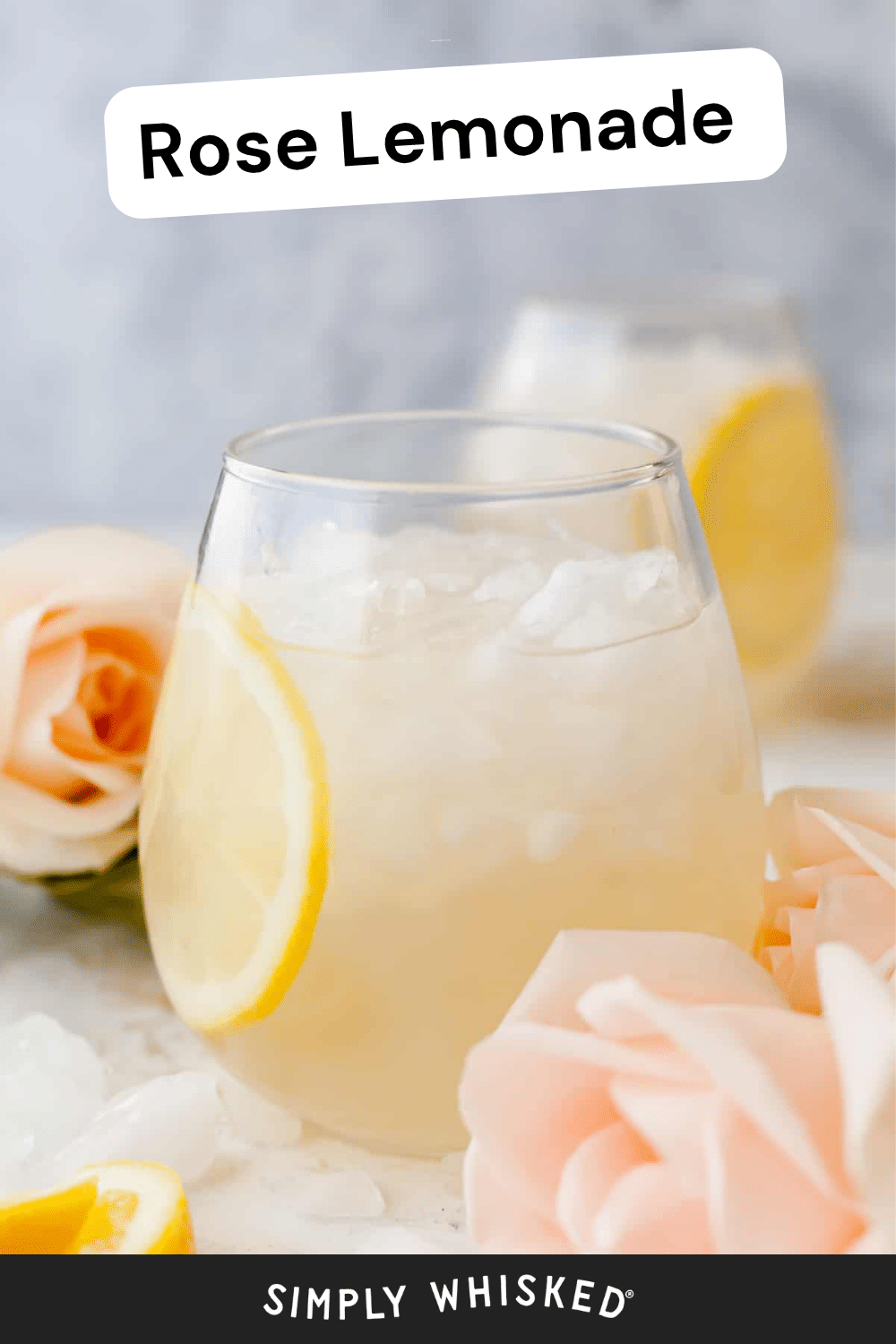 A refreshing glass of rose lemonade with ice and a lemon slice, surrounded by pink roses and lemon wedges on a white surface.