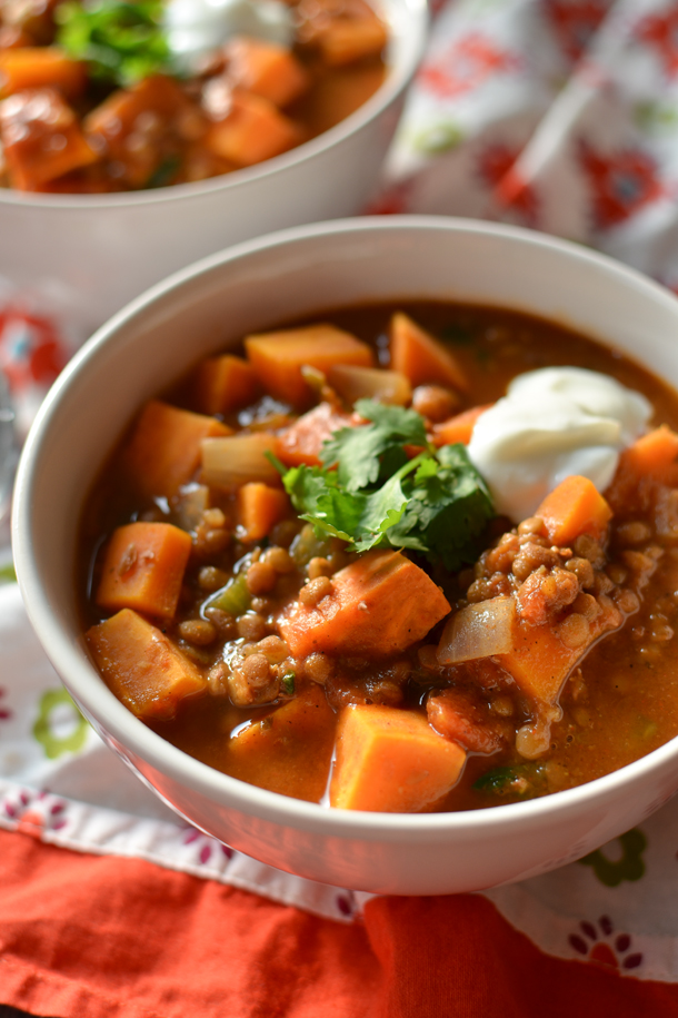 close up view of sweet potato lentil chili with garnish and dollop of sour cream in a medium white bowl