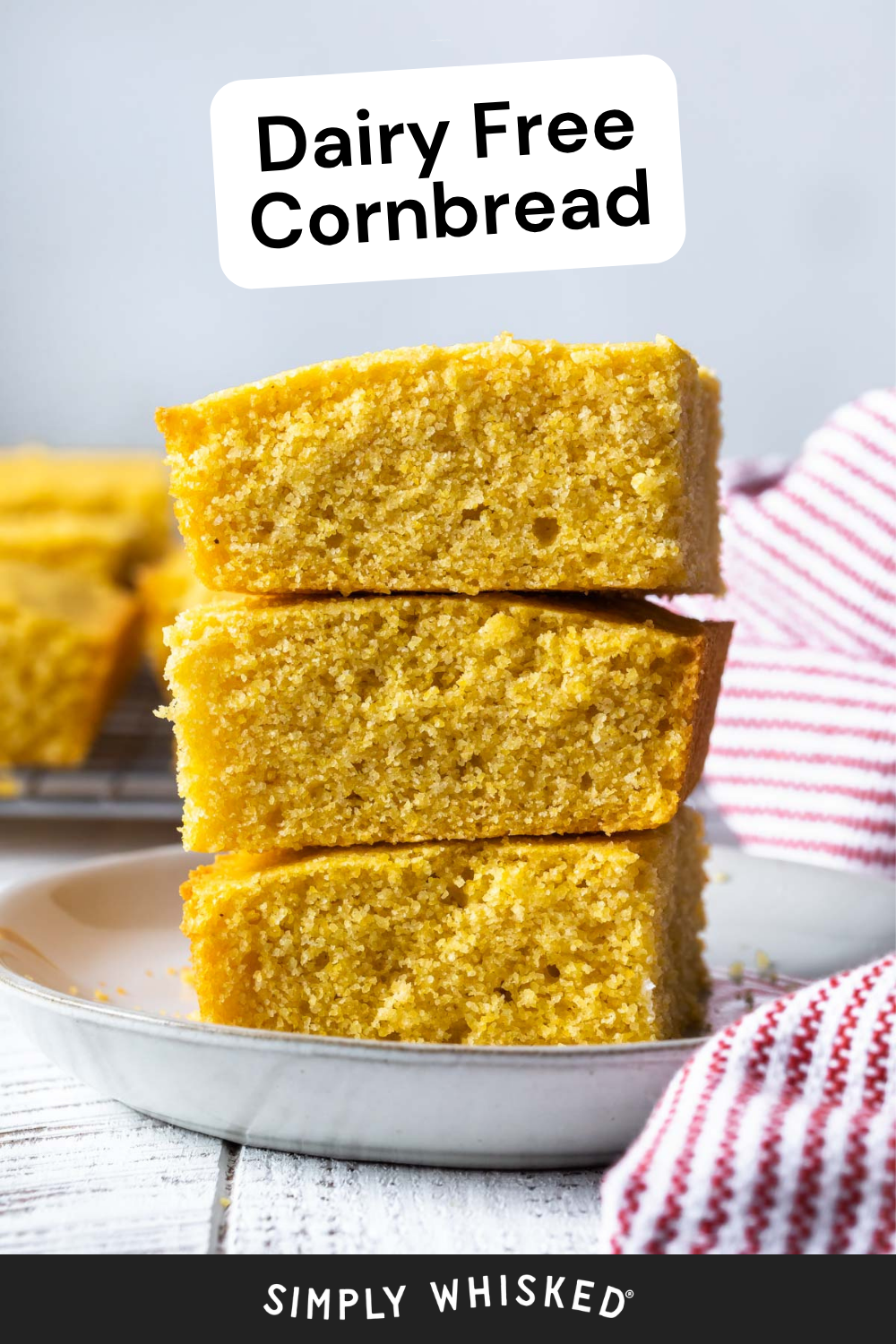 Three slices of golden dairy free cornbread stacked on a white plate, with a red striped towel nearby. Text at the top reads Dairy Free Cornbread.