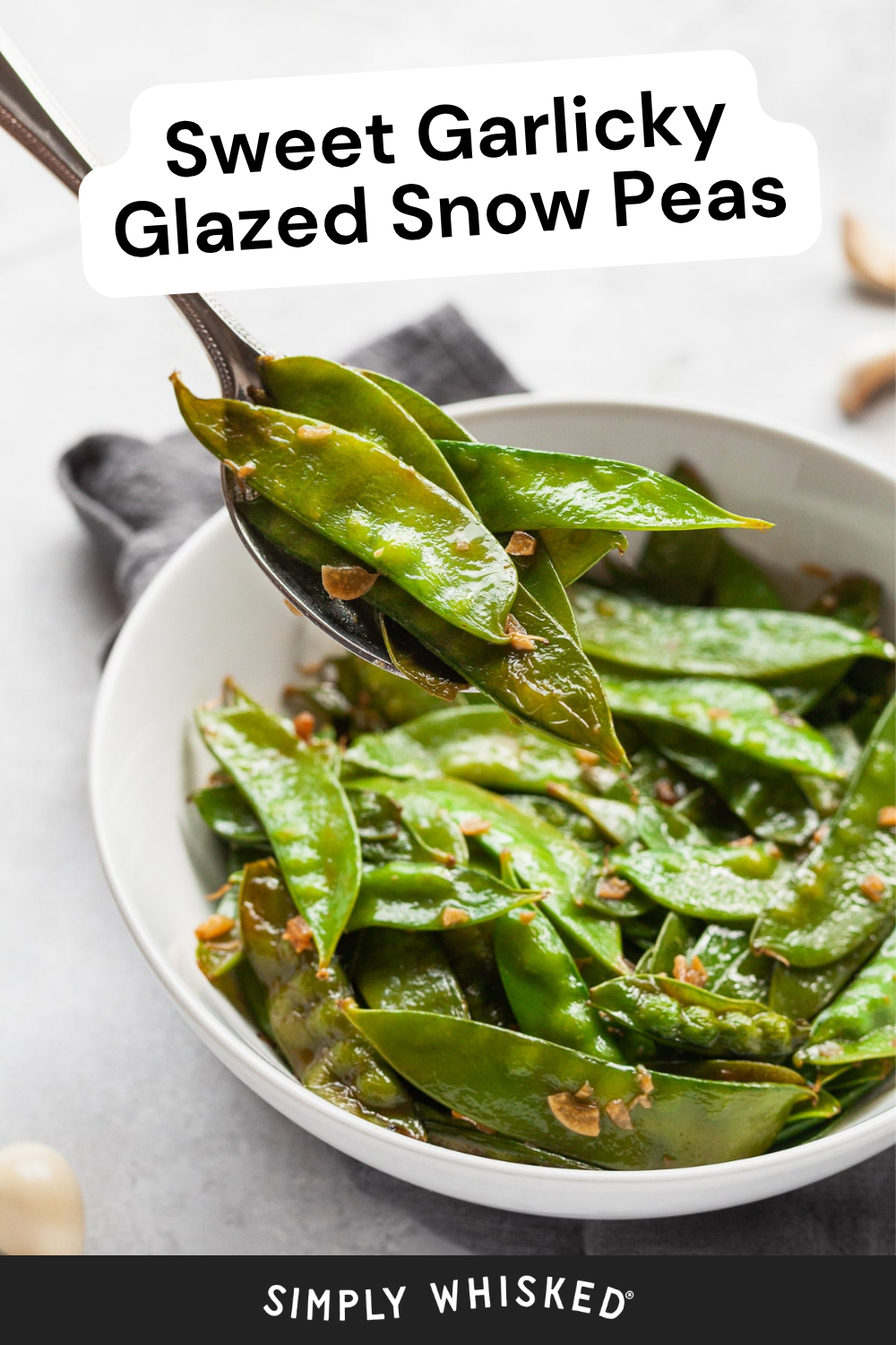 A spoon lifts sweet, glazed snow peas from a white bowl. The peas are shiny and garnished with bits of garlic. Text reads Sweet Garlicky Glazed Snow Peas.