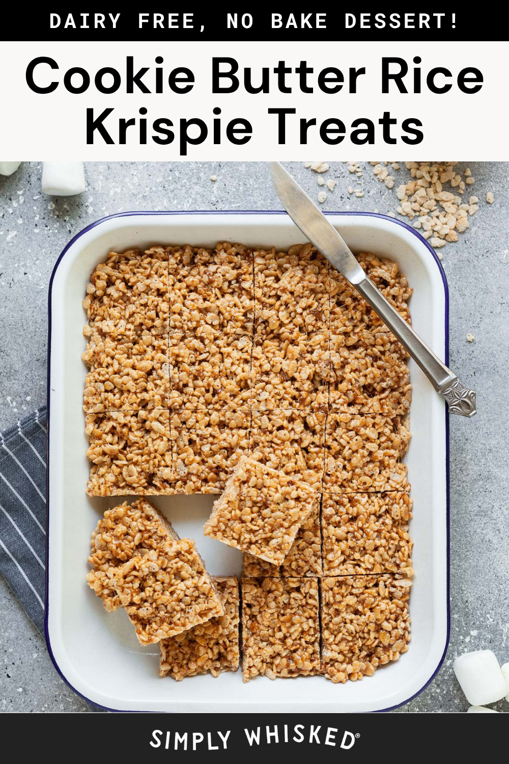 A baking dish filled with decadent cookie butter treats in the form of rice krispie squares, most cut and ready to serve, with a serving spatula and some treats already removed. Marshmallows and rice cereal are scattered nearby for an inviting, homemade touch.