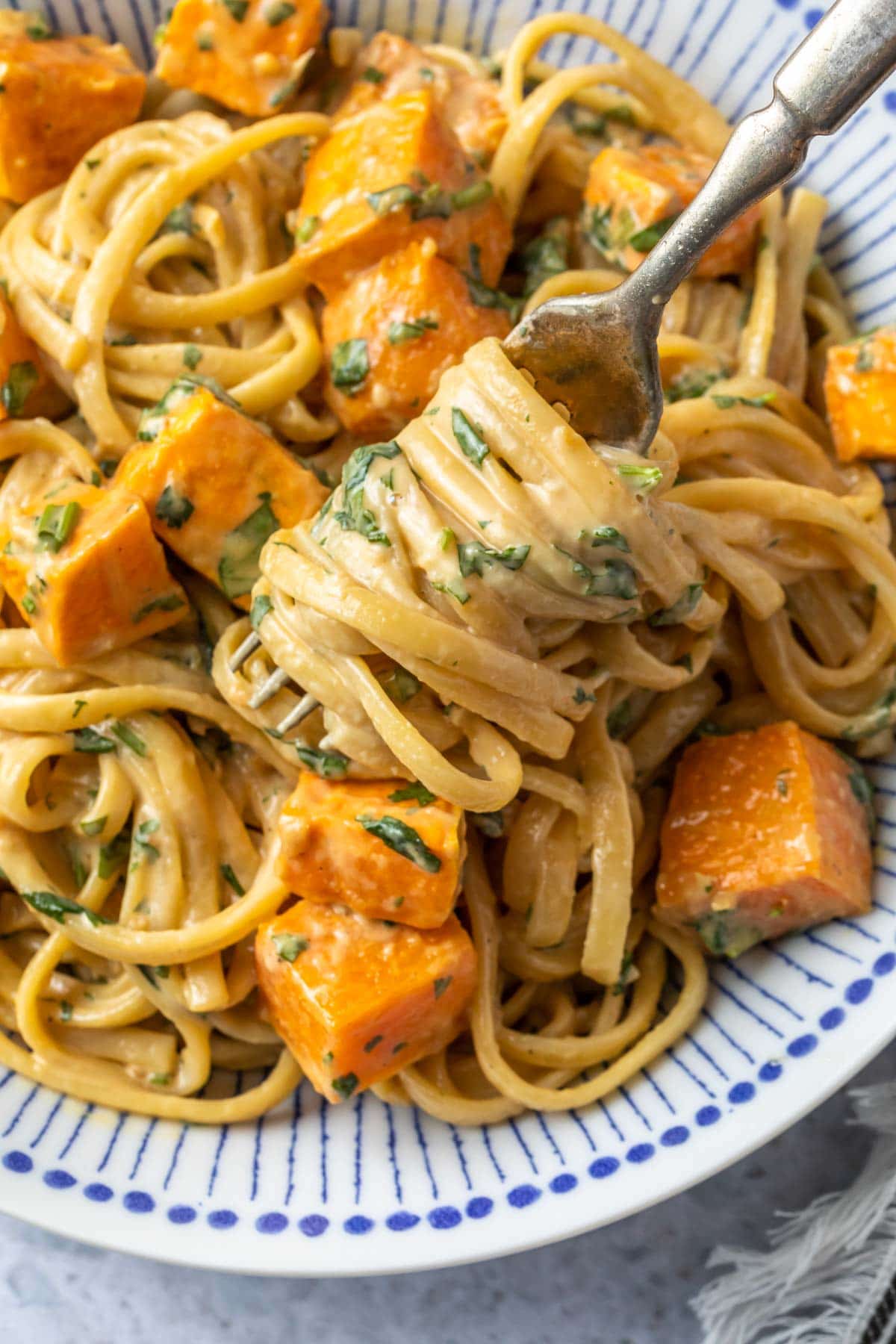 close up of sweet potato pasta twirled on a fork with creamy tahini sauce
