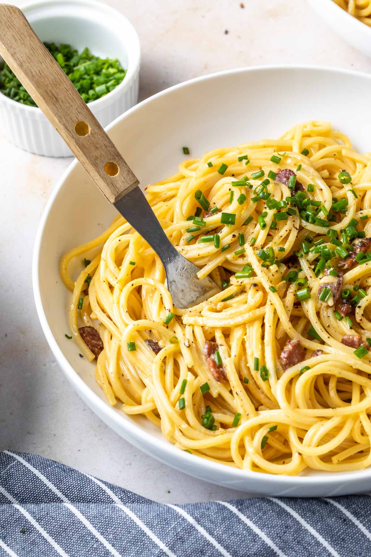 carbonara pasta with bacon and chives in a white bowl