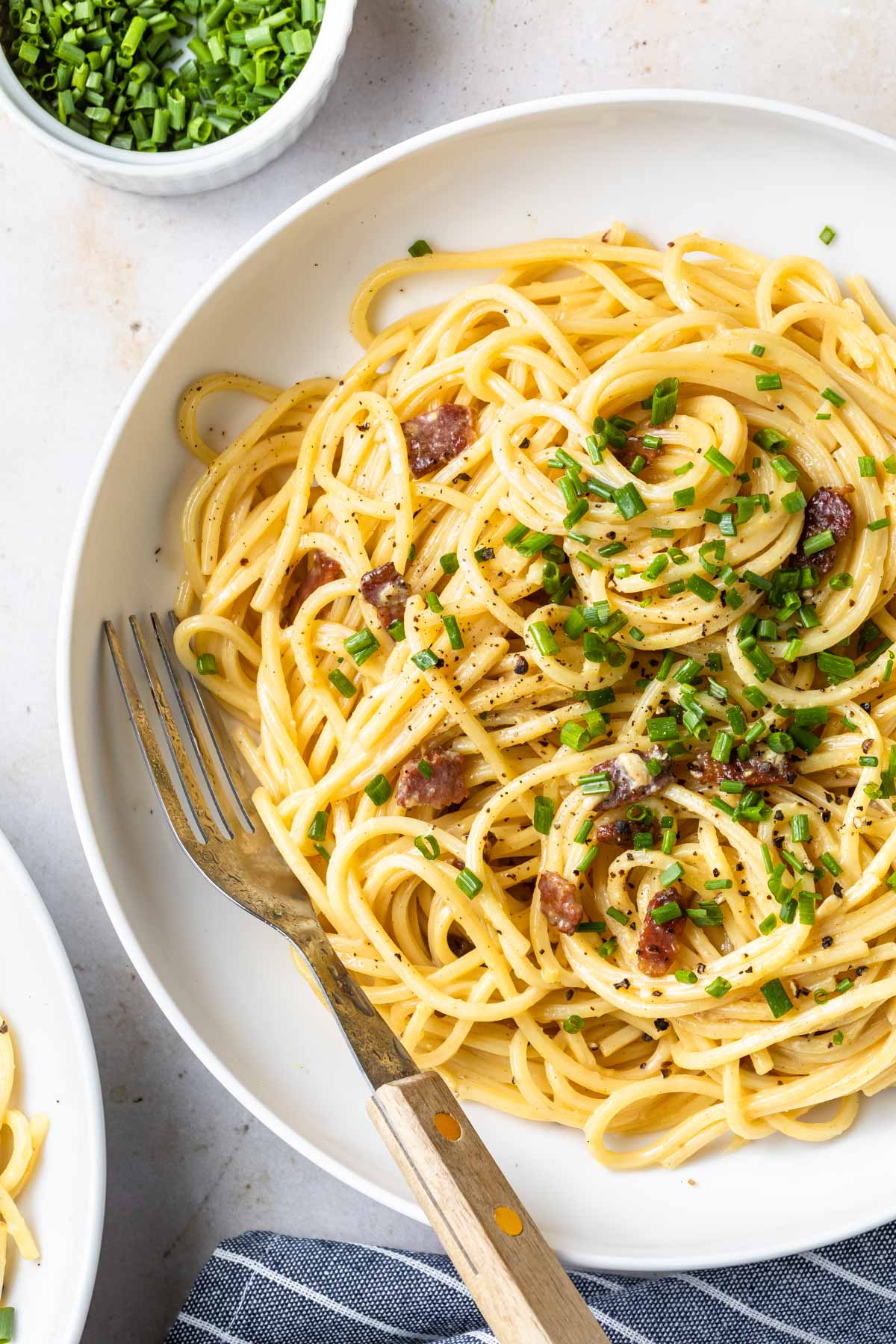 carbonara pasta with bacon and chives in white bowl