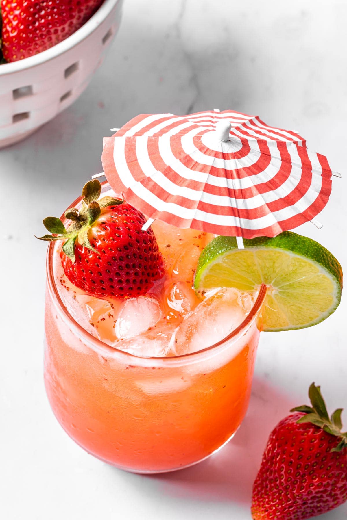 A strawberry mocktail mule garnished with a cocktail umbrella, lime wheel and a strawberry. 