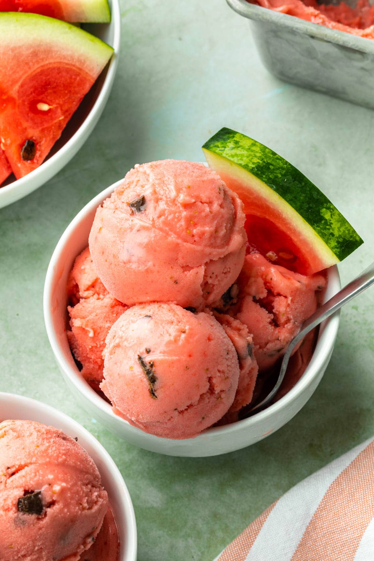 Watermelon sorbet in a bowl with a watermelon wedge and a spoon. 