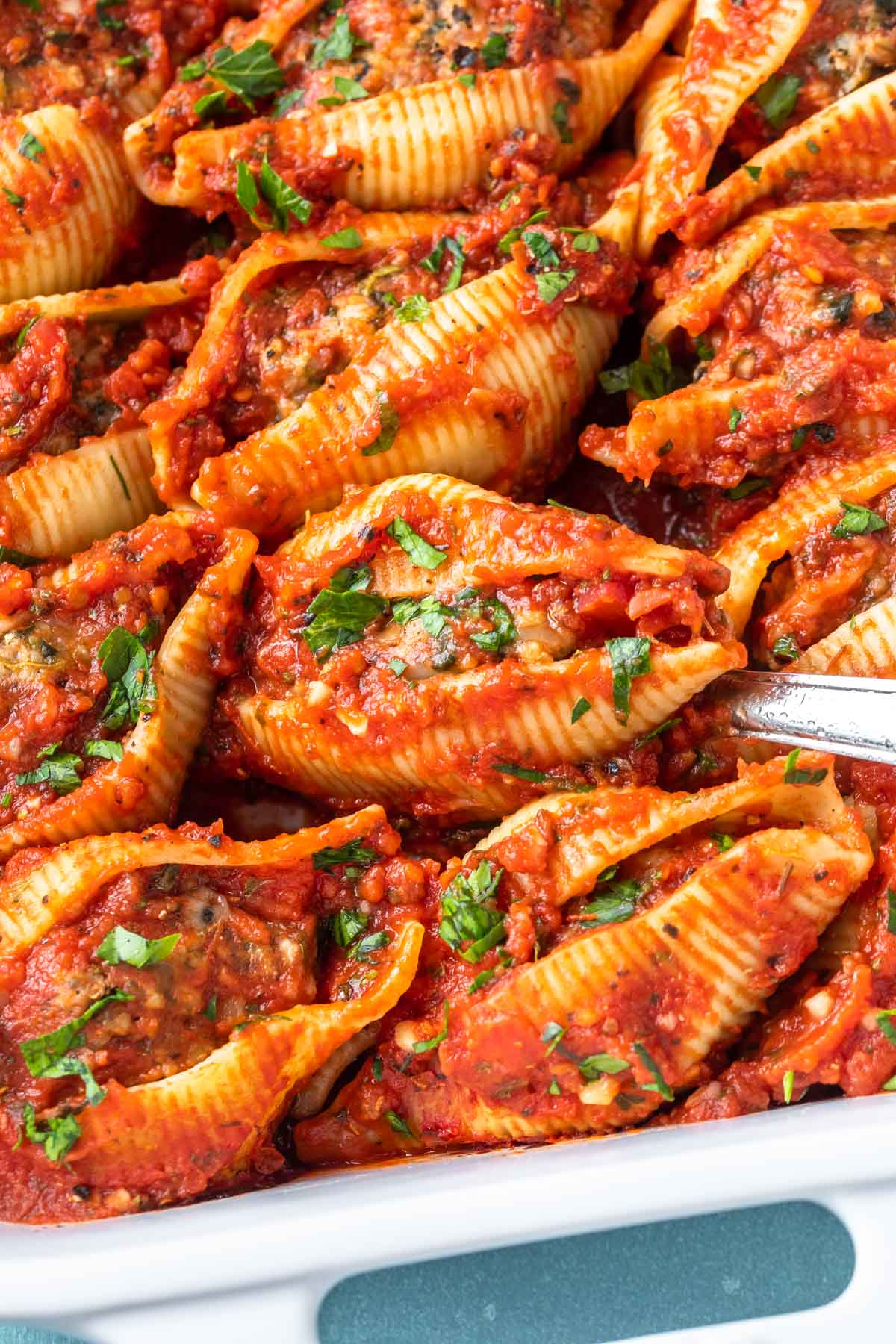 overhead close up of meat stuffed shells in a baking dish being scooped by a spoon
