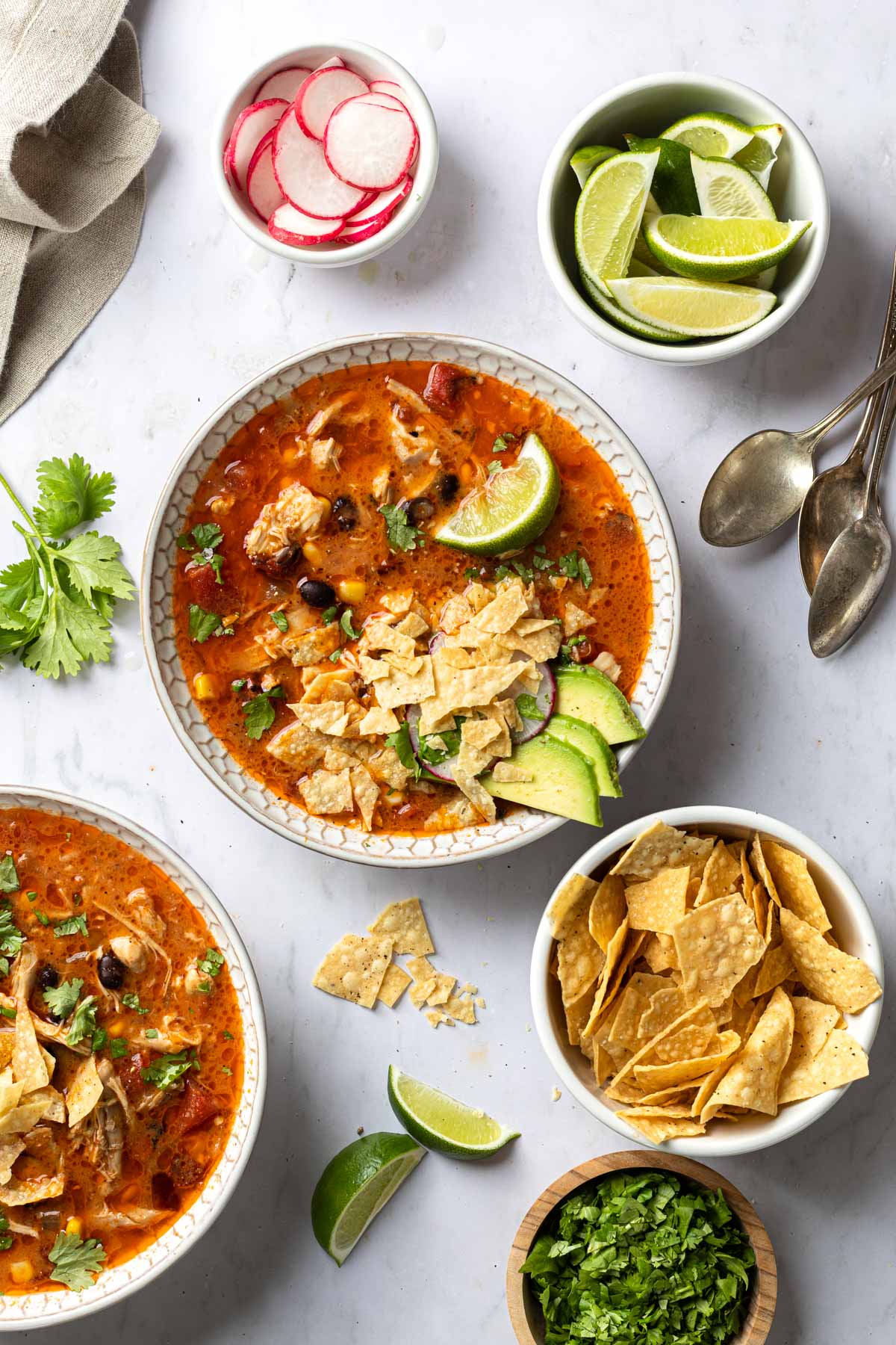 Overhead shot of a few bowls of tortilla soup and various garnishes surrounding them. 