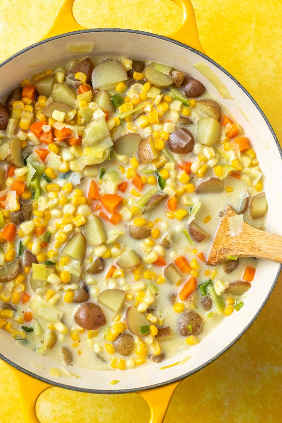 overhead view of potato corn chowder in a large dutch oven with a stirring spoon