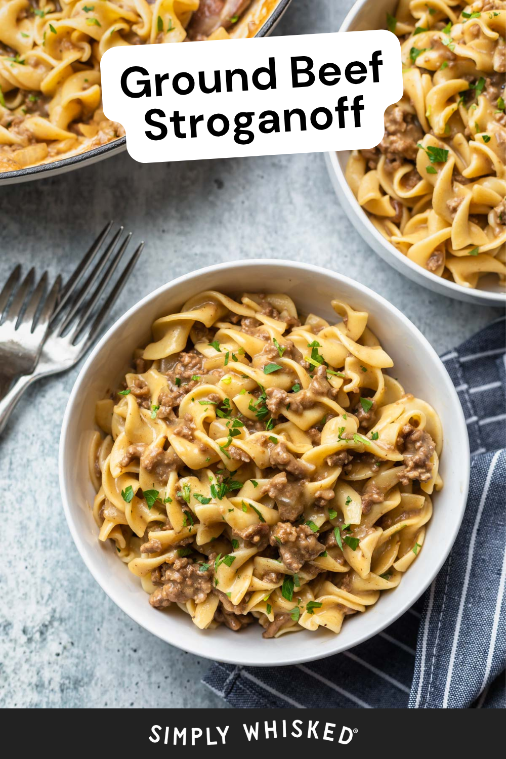 A white bowl filled with creamy ground beef stroganoff on egg noodles, garnished with chopped parsley, sits next to a fork and a blue napkin.