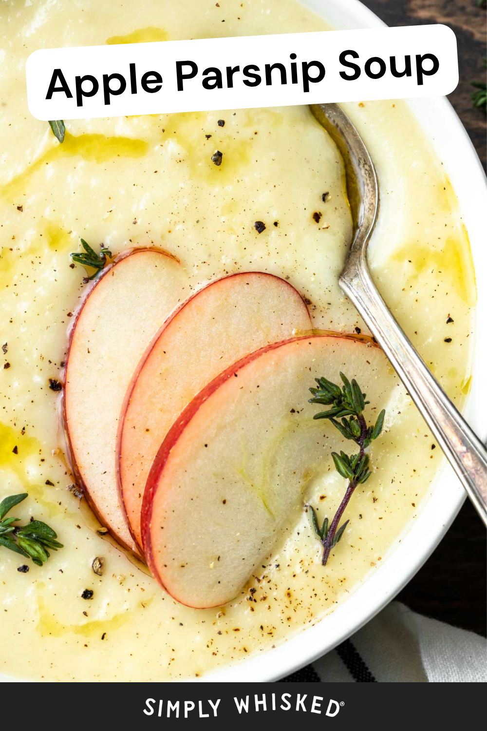 A bowl of creamy apple parsnip soup is garnished with thin apple slices, fresh thyme, black pepper, and a drizzle of oil. A spoon rests in the comforting apple parsnip soup, ready to enjoy.