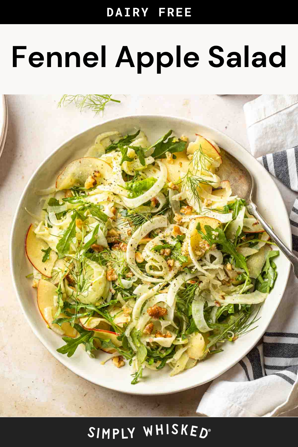 A vibrant bowl of fennel apple salad with arugula, thin apple slices, chopped nuts, and fresh herbs is served with a fork and a striped napkin on the side.