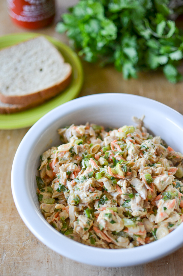 spicy chicken salad in a bowl with bread on a plate in the background. 