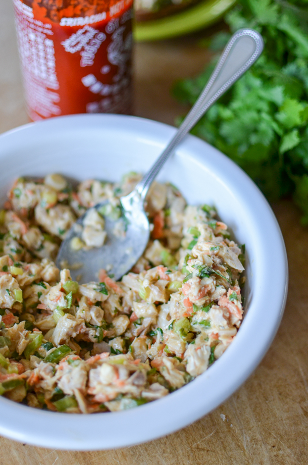 a bowl of spicy chicken salad with a bottle of sriracha in the background. 